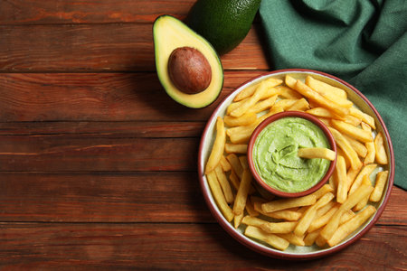 Plate with french fries, guacamole dip and avocado served on wooden table, flat lay. Space for textの写真素材