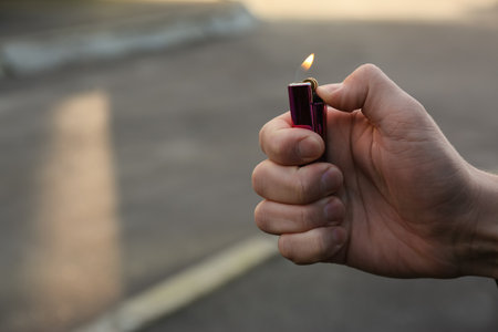 Man holding lighter with burning flame outdoors, closeup. Space for textの写真素材