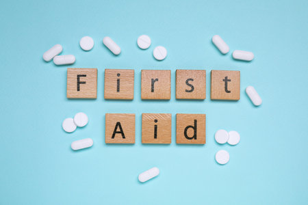 Words First Aid made of wooden cubes and pills on light blue background, flat layの写真素材