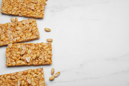Delicious peanut bars (kozinaki) and nuts on white marble table, flat lay. Space for textの写真素材