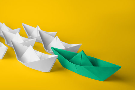 Group of paper boats following green one on yellow background. leadership conceptの写真素材