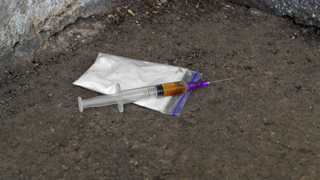 Plastic bag with powder and syringe on asphalt outdoors. hard drugsの写真素材