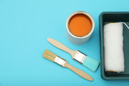 Can of orange paint, brushes, roller and container on turquoise background, flat lay. Space for textの写真素材