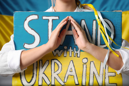 Woman holding poster with words Stand with Ukraine near national flag, closeupの写真素材