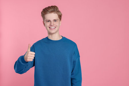 Teenage boy showing thumb up on pink background. Space for textの写真素材