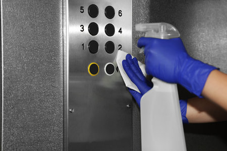 Woman wiping buttons of elevator`s panel with detergent and paper napkin, closeup