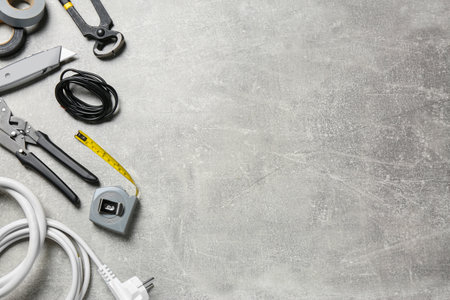New wires and electrician's tools on gray table, flat lay. Space for text