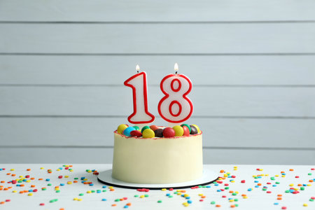 Coming of age party - 18th birthday. Delicious cake with number shaped candles on white tableの写真素材
