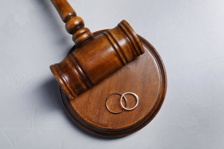 Divorce process. Wooden gavel and wedding rings on gray textured table, flat layの写真素材