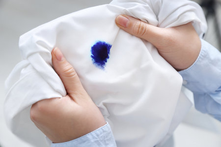 Woman holding white shirt with blue ink stain on blurred background, closeupの写真素材
