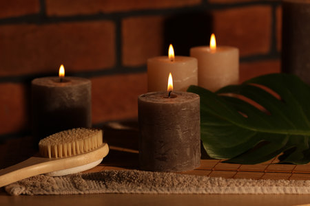 Spa composition with burning candles, massage brush and monstera leaf on wooden table near red brick wallの写真素材