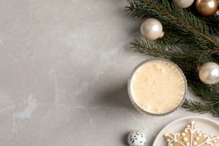 Glass of delicious eggnog and decorated fir branch on light marble table, flat lay. Space for text
