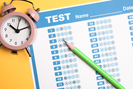 Answer sheet, pencil and alarm clock on yellow background, flat lay. student passing exam