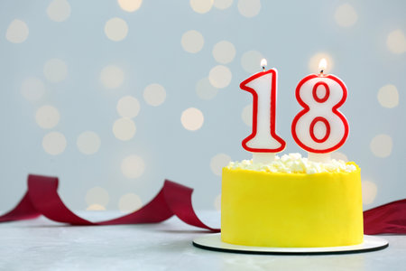 Coming of age party - 18th birthday. Delicious cake with number shaped candles on white table against blurred lights, space for textの写真素材