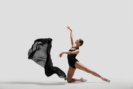 Graceful young ballerina practicing dance moves with black veil on white backgroundの写真素材