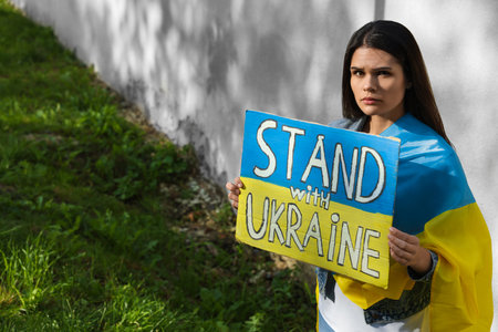 Sad woman holding poster in colors of national flag and words Stand with Ukraine outdoors. Space for textの写真素材