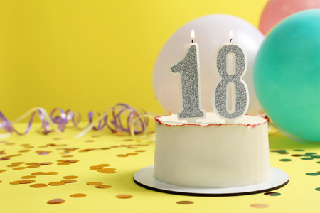 Coming of age party - 18th birthday. Delicious cake with number shaped candles on yellow background, space for textの写真素材