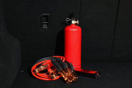 Red fire extinguisher and battery jumper cables in trunk. car safety