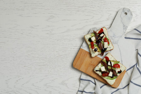 Delicious sandwiches with anchovy, cheese and tomato on white wooden table, top view. Space for textの写真素材