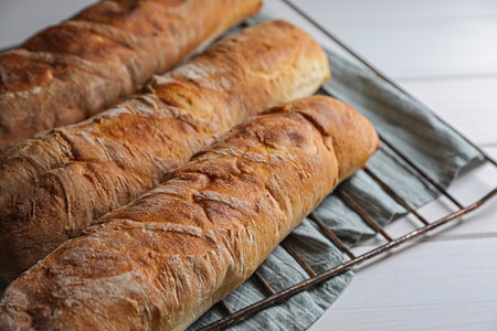 Fresh crispy ciabattas on white wooden table, closeup. Space for text