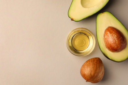 Cooking oil in bowl and fresh avocados on light gray background, flat lay. Space for text