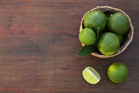 Fresh ripe limes and wicker basket on wooden table, flat lay. Space for textの写真素材