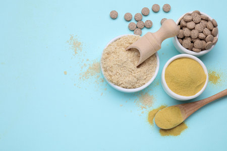 Beer yeast powder, flakes and pills on light blue background, flat lay. Space for text