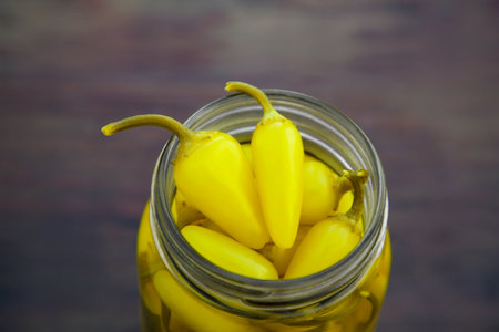 Glass jar of pickled yellow jalapeno peppers on wooden table, closeupの写真素材