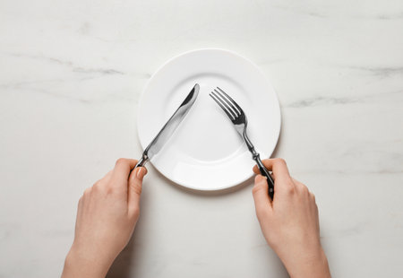 Woman with empty plate and cutlery at white marble table, top viewの写真素材