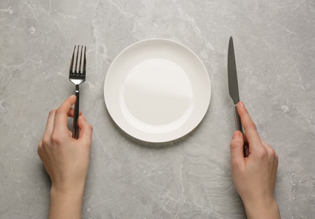 Woman with empty plate and cutlery at light gray table, top viewの写真素材