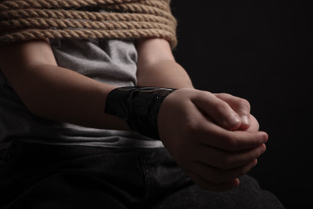 Little boy tied up and taken hostage on dark background, closeupの写真素材