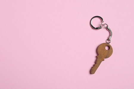 Wooden keychain in shape of key on pale pink background, top view. Space for textの写真素材