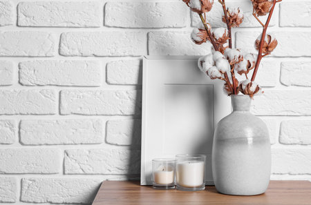Cotton branches with fluffy flowers in vase on wooden table near white brick wall. Space for textの写真素材
