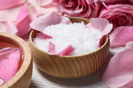 Bowl with sea salt and beautiful petals of roses on white wooden table, closeupの写真素材