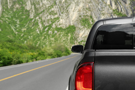 Picturesque view of big mountains and trees near road with black car, space for textの写真素材
