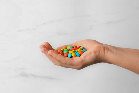 Woman with handful of tasty colorful candies on white marble background, closeupの写真素材