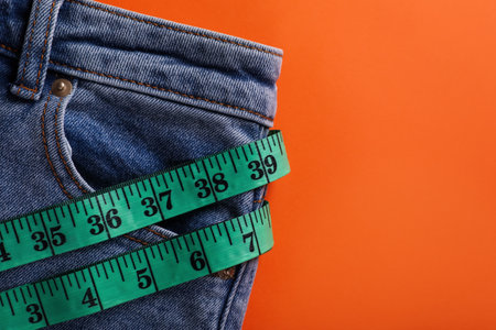 Jeans and measuring tape on orange background, top view with space for text. weight loss conceptの写真素材