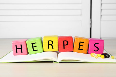 Word Herpes made of colorful cubes, open book and pills on beige tableの写真素材
