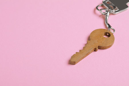 Wooden keychain in shape of key on pale pink background, closeup. Space for textの写真素材