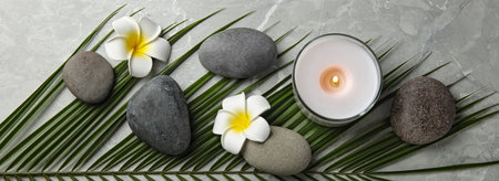 spa treatments. Flat lay composition with stones, plumeria flowers and burning candle on gray table....