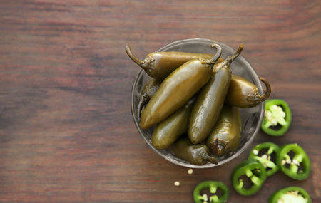 Fresh and pickled green jalapeno peppers on wooden table, flat lay. Space for textの写真素材