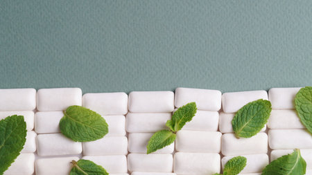 Tasty chewing gums and fresh mint leaves on gray background, flat lay. Space for textの写真素材