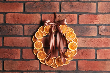 Decorative wreath made with dry oranges and ribbon hanging on red brick wallの写真素材