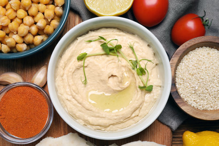 Delicious hummus with microgreens and different ingredients on wooden table, flat layの写真素材