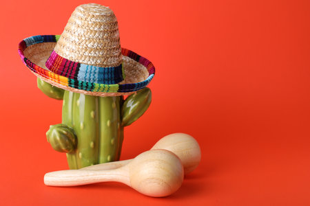 Wooden maracas and toy cactus with sombrero hat on red background, space for text. musical...
