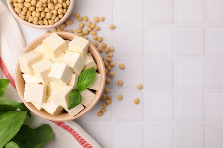 Delicious tofu cheese, basil and soybeans on white tiled table, flat lay. Space for textの写真素材