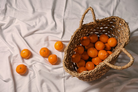 Stylish wicker bag with ripe tangerines on white bedsheet, flat layの写真素材