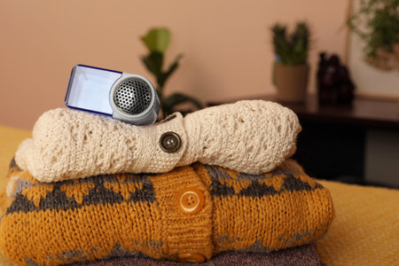 Modern fabric shaver and knitted clothes on orange blanket indoors, closeupの写真素材