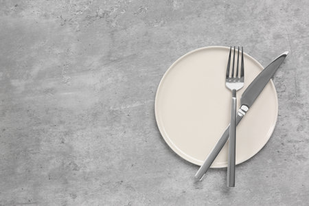 Clean plate with cutlery on light gray table, flat lay. Space for text