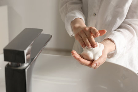 Woman washing hands with cleansing foam near sink in bathroom, closeup